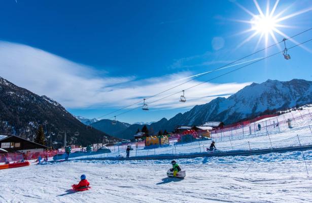 Bambini giocano sulla neve sotto il sole in montagna.