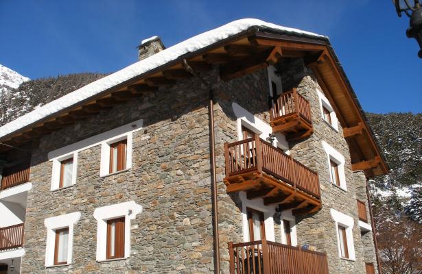 Chalet di montagna in pietra con balconi in legno, coperto di neve.