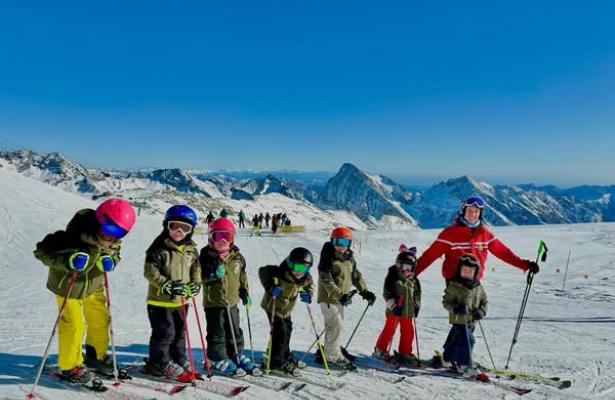 Bambini sciatori in fila con istruttore sulle Alpi.