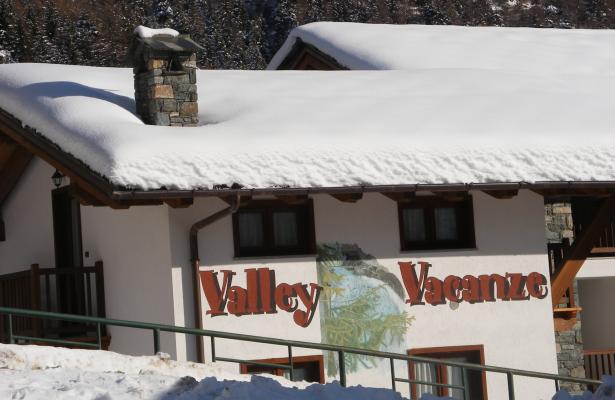 Chalet innevato con insegna 'Valley Vacanze' tra le montagne.