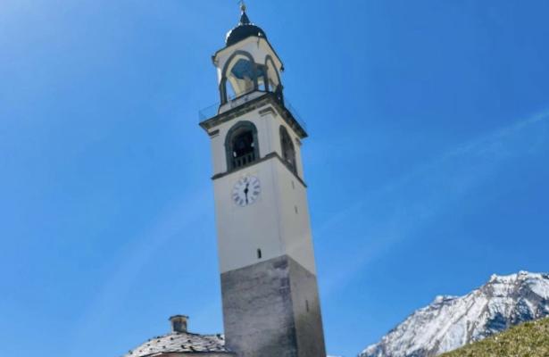 Bell tower in mountains with blue sky and snow.