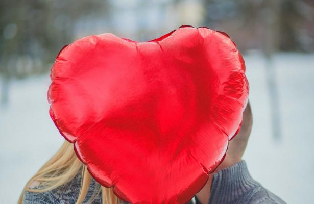 Couple with heart-shaped balloon, outdoors in winter.